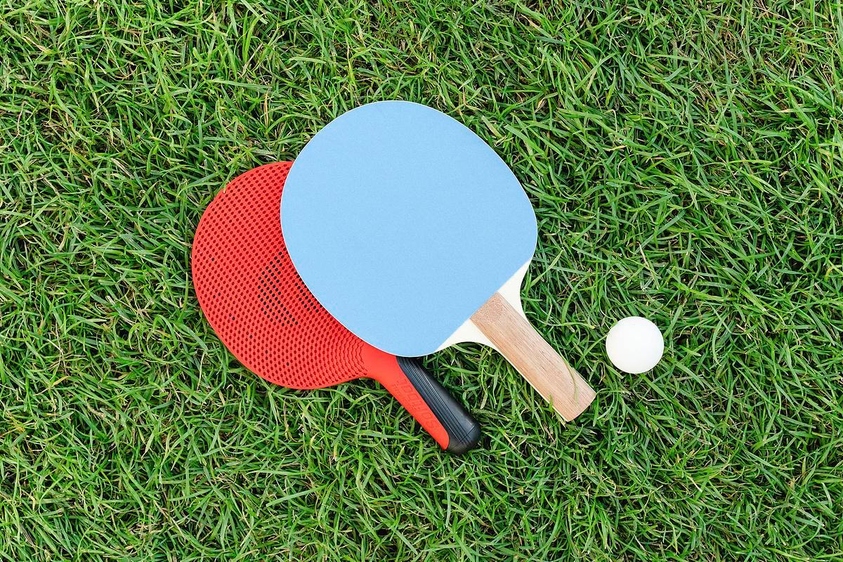 Титульное изображение проекта. Фото: на зеленой траве лежат две ракетки (красная и голубая) и белый мячик для игры в настольный теннис