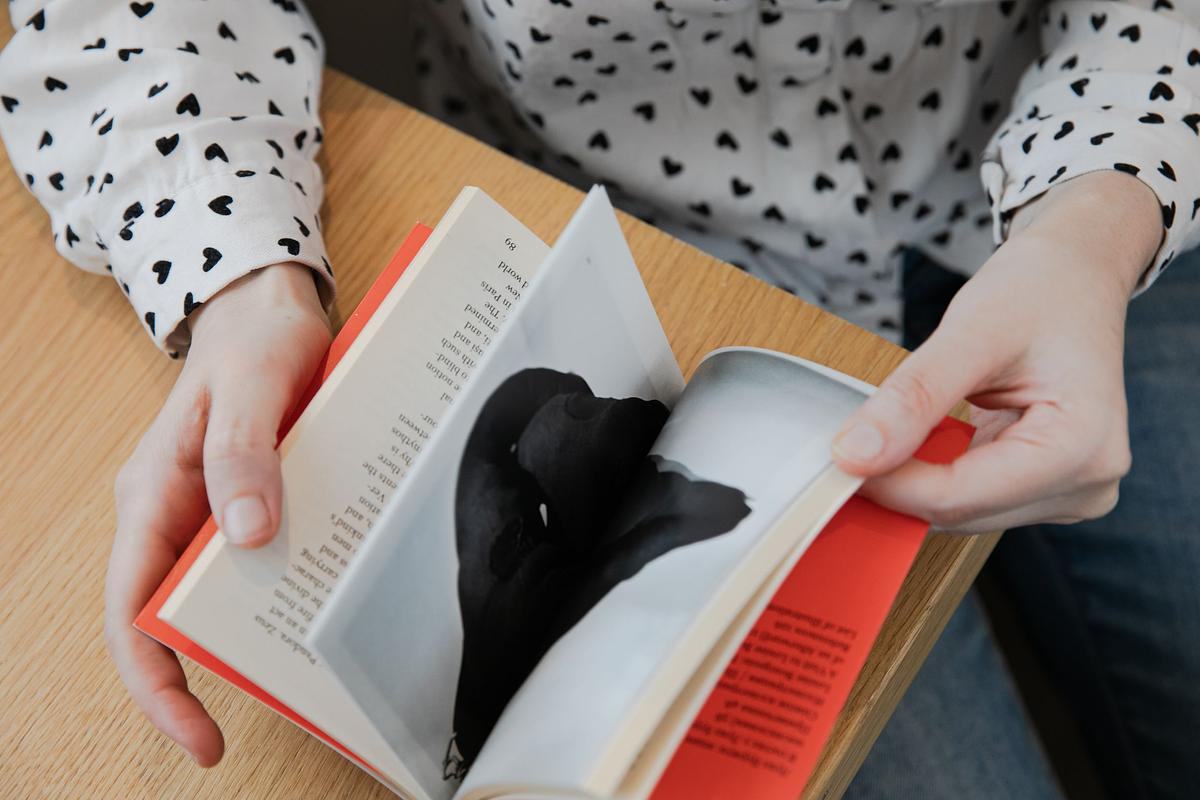 Титульное изображение для страницы события: руки держат полураскрытой книгу с красной обложкой на развороте с черной иллюстрацией