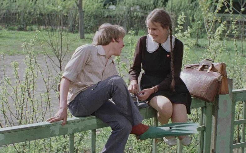 Кадр из фильма «Не болит голова у дятла», школьница и школьник сидят на заборе на фоне деревьев