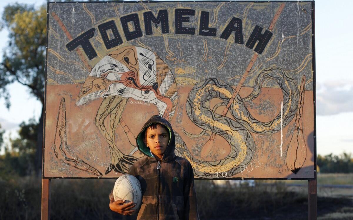 Кадр из фильма «Тумела», мальчик с мячом для рtu,b на фоне билборда с надписью Toomelah