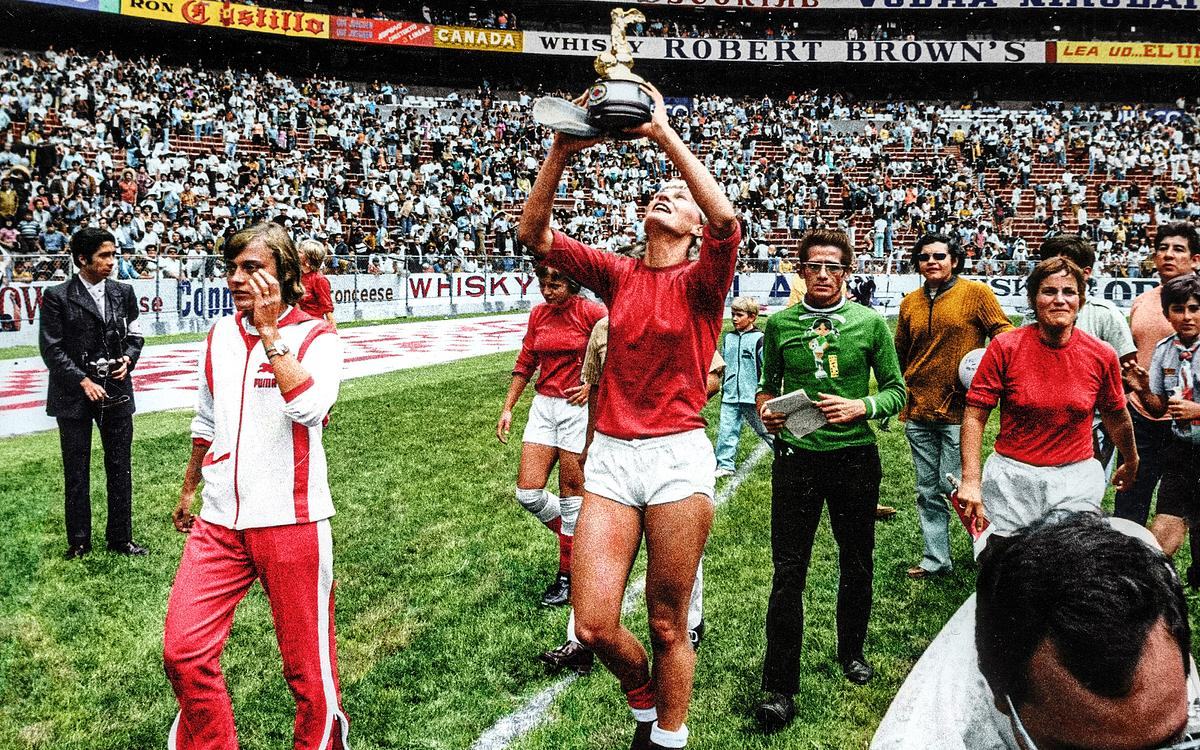 Кадр из фильма «COPA 71». Цветная фотография: женская футбольная команда идет по полю стадиона, первая женщина несет в руках победный кубок