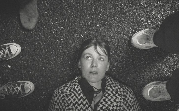 Девушка лежит на асфальте и смотрит на окружающих ее людей