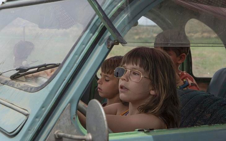 Кадр из фильма «Земля Алькаррас », девочка сидит за рулем машины, полной других детей