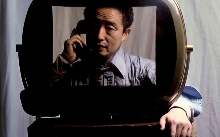 Кадр из фильма «Нам Джун Пайк: Луна — первый телевизор», мужчина с телефонной трубкой у уха сидит в раме в виде экрана телевизора