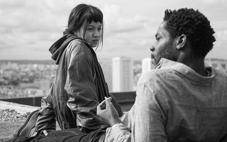 Кадр из фильма «Париж, 13-й округ»,  женщина и мужчина сидят на крыше, женщина смотрит на мужчину, а он в сторону