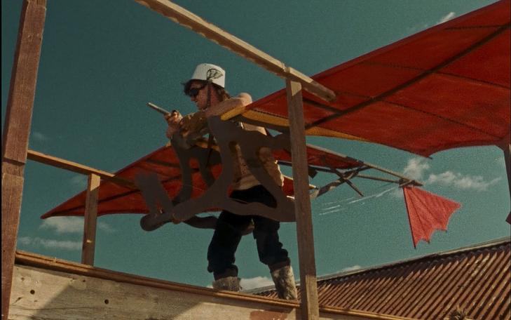 Кадр и фильма «Духи воздуха и облачные гремлины», мужчина стоит на крыше дома в самодельном летательном аппарате