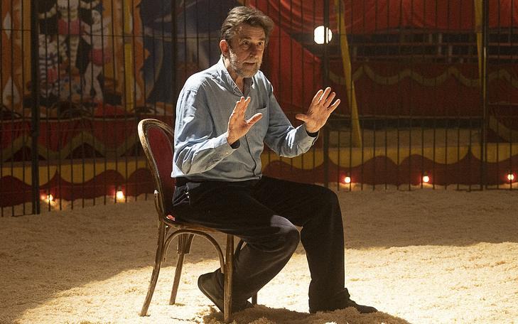 Кадр из фильма «Великая магия», мужчина сидит на стуле в центре цирковой арены и ведет рассказ с жестикуляцией