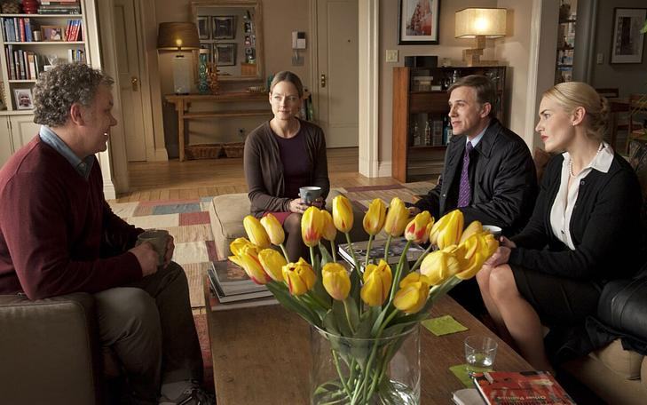 Кадр из фильма «Резня», два мужчины и две женщины сидят за круглым столом с букетом желтых тюльпанов в вазе и разговаривают