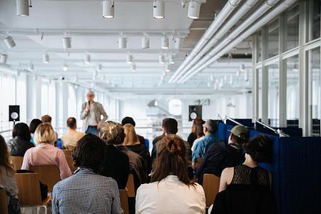 Человек с микрофоном делится своей лекцией с аудиторией, сидящей на стульях