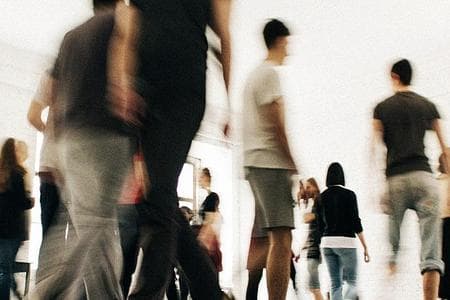 Много людей в одежде спортивного стиля находятся в зале с белыми стенами и полом