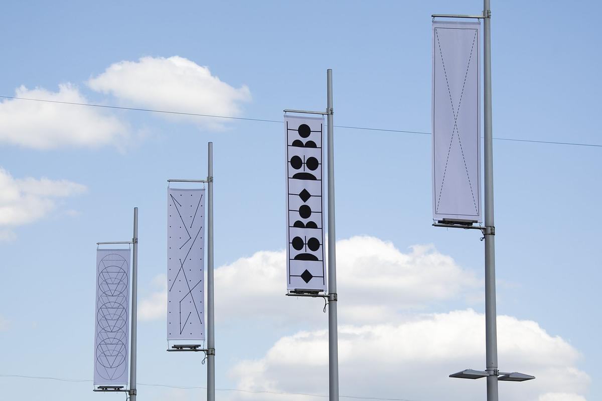 Титульное изображение для страницы события: флагштоки с вертикальными прямоугольными знаменами с фирстилем выставок ГЭС-2 на фоне голубого неба