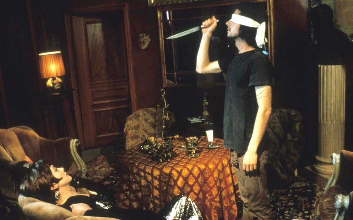 Титульное изображение для страницы события: кадр из фильма «Генеалогия преступления», мужчина с завязанными белой лентой глазами стоит с ножом перед сидящей в кресле женщиной