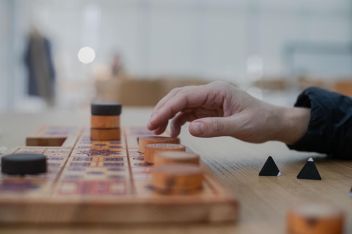 Титульное изображение для страницы события: рука тянется к белой деревянной шашке на доске