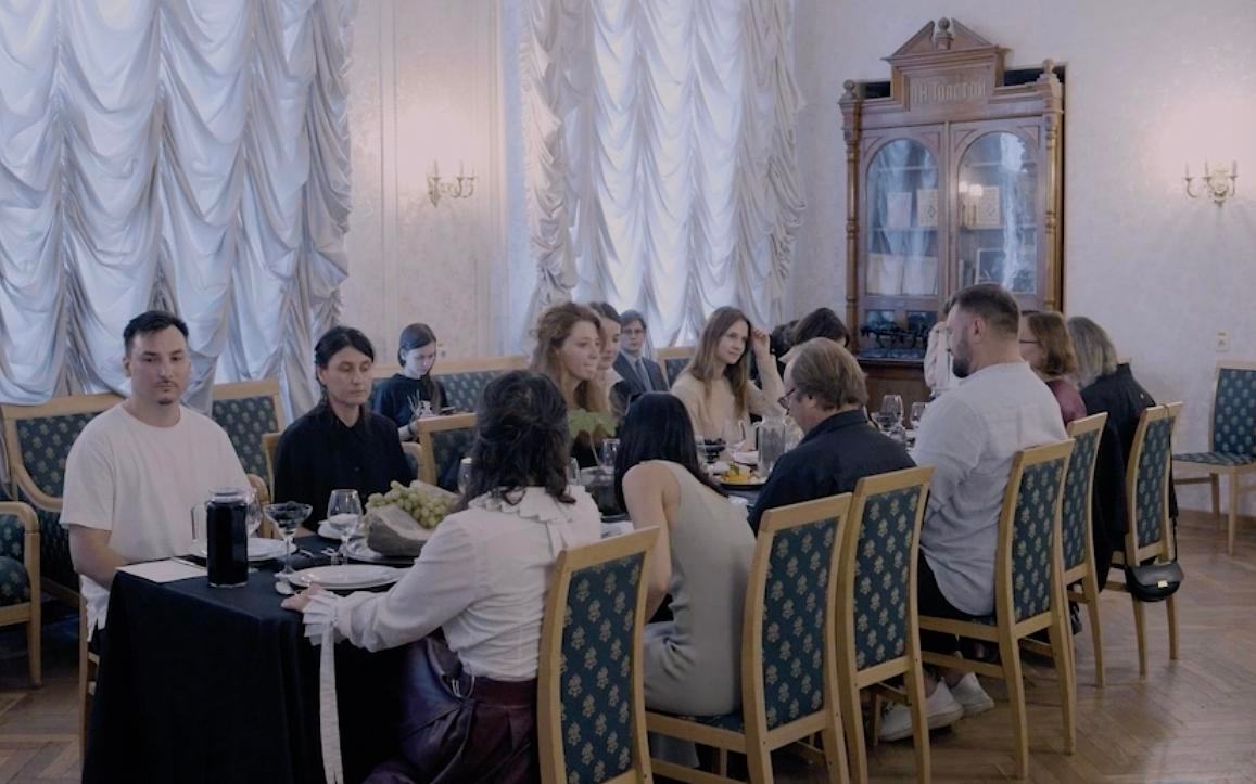 Титульное изображение для страницы события: кадр из фильма «Овражьи проводы», люди сидят за длинным столом в помпезном помещении