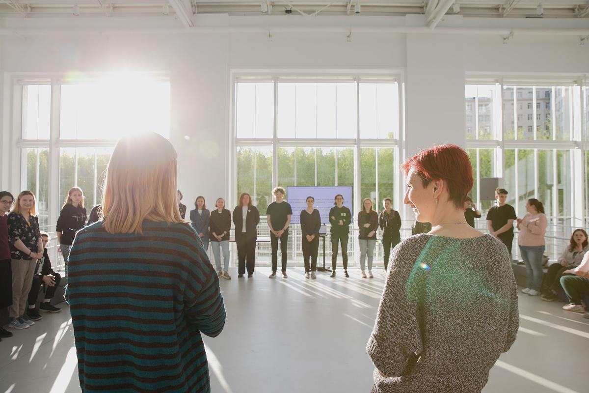 Титульное изображение для страницы события: люди стоят в кругу на платформе ГЭС-2, в окно светит солнце