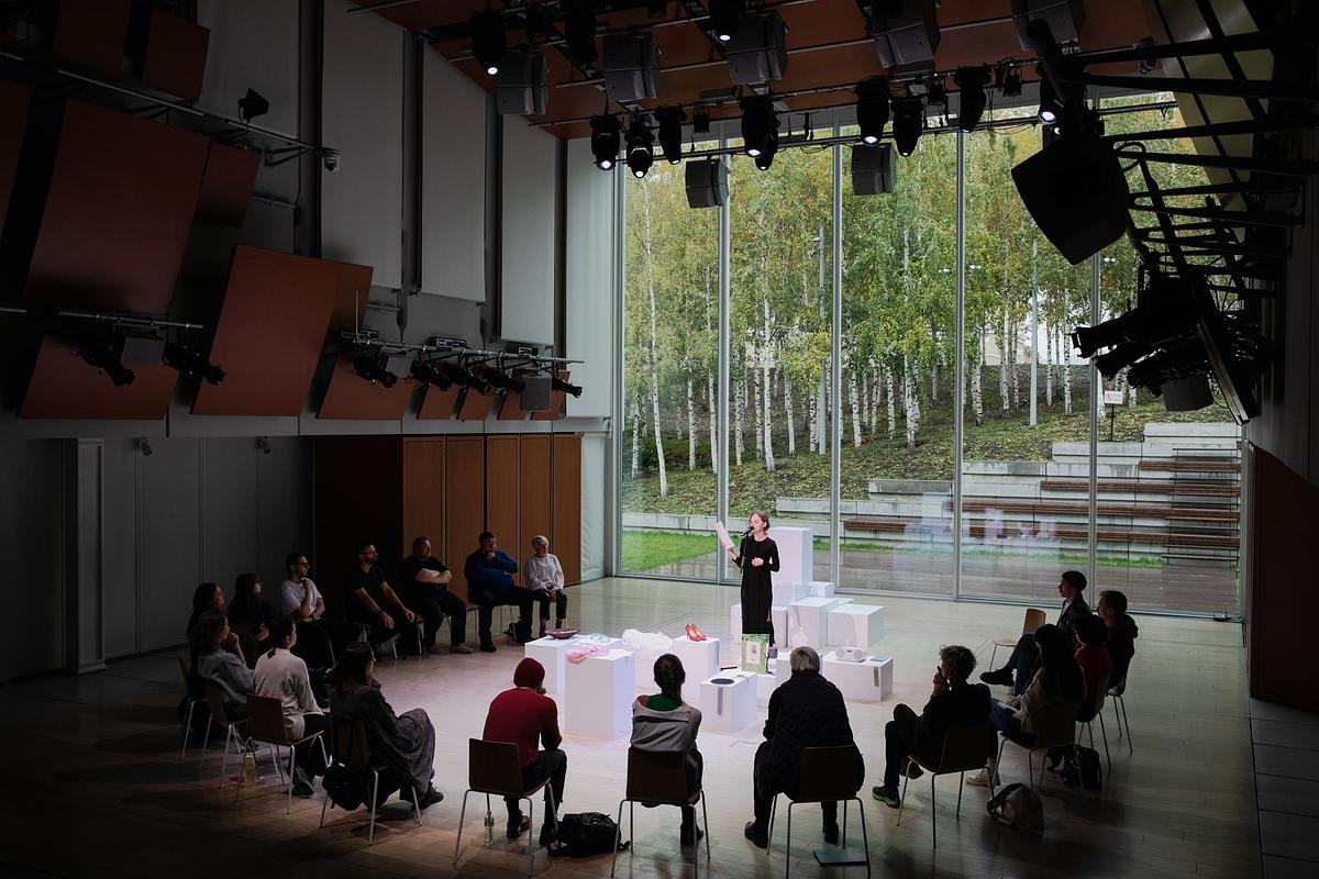 Два человека стоят друг напротив друга на сцене в окружении стульев