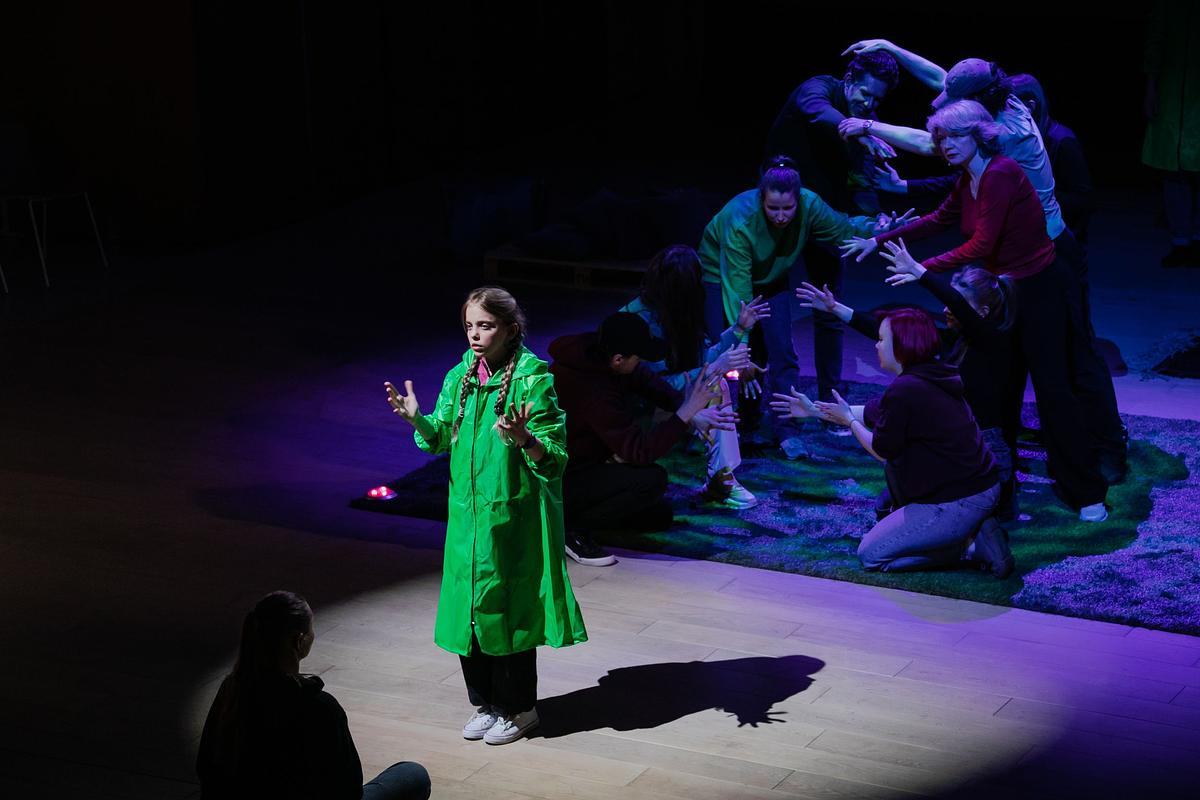 Девушка в зеленом пальто выступает на сцене на фоне пар актеров