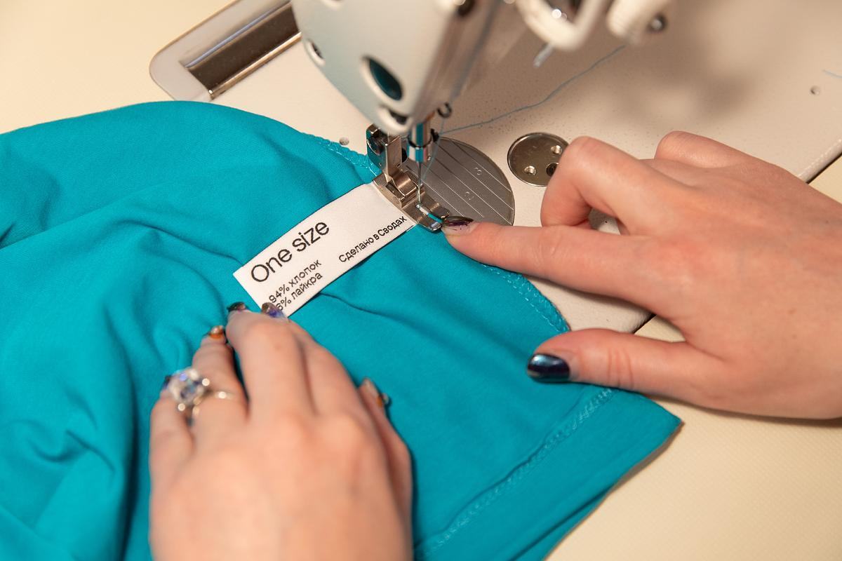Руки пришивают бирку к синей футболке за швейной машинкой