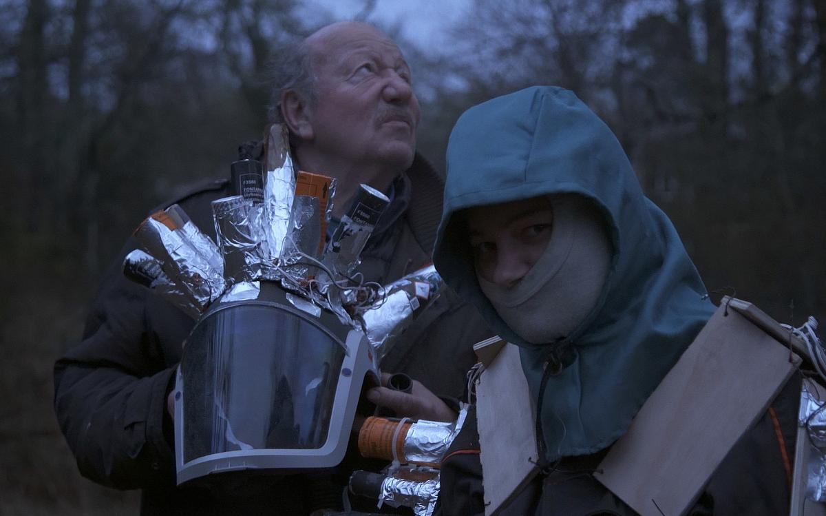 Кадр из фильма «Огненная земля», два человека с шлемами в вечернем лесу