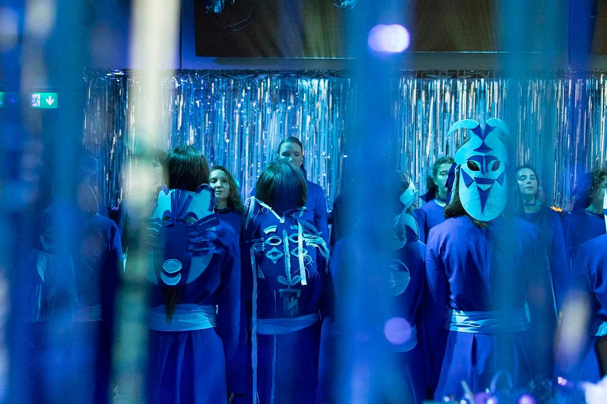 Люди в синем стоят в два ряда в окружении мишуры