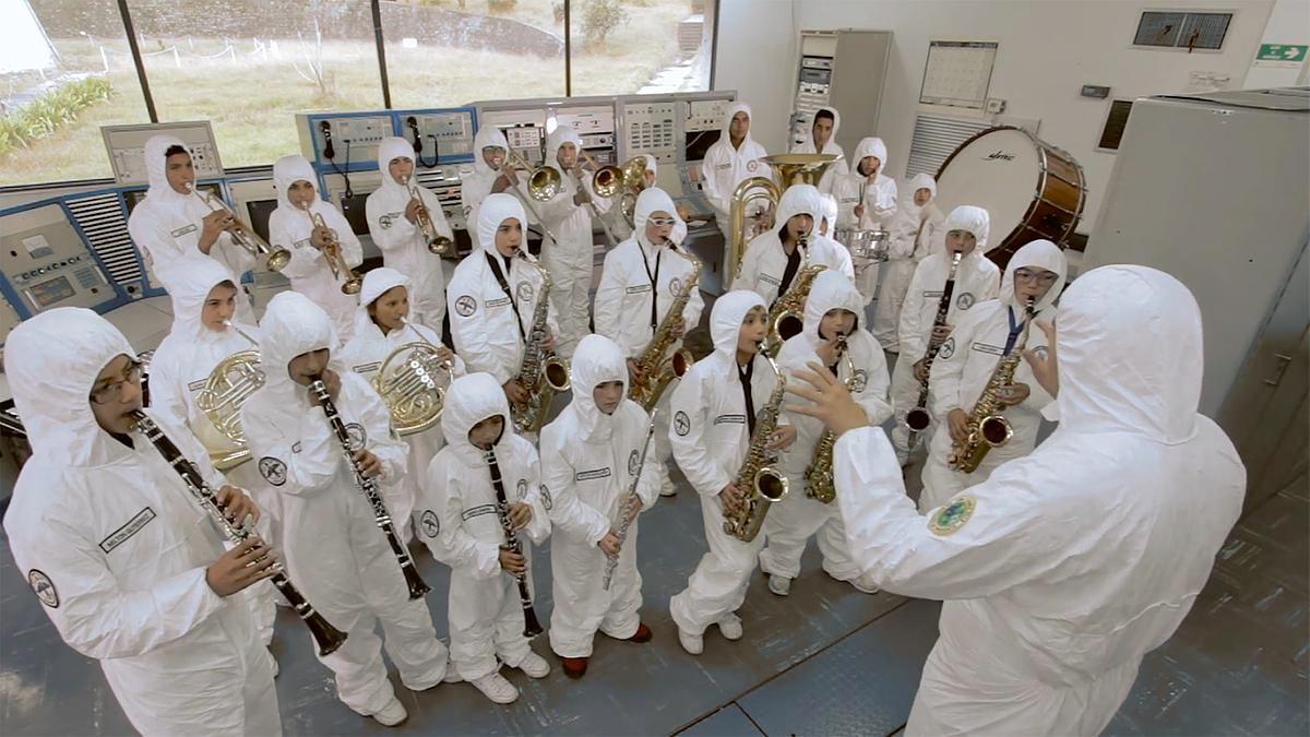 Группа людей в хазмат-костюмах играют на духовых