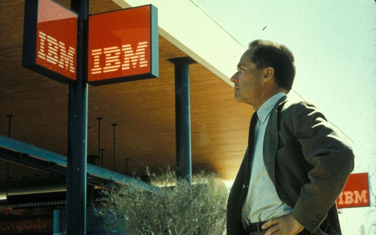 Кадр из фильма «Модернизм, Inc.», человек в костюме стоит под вывеской "IBM"