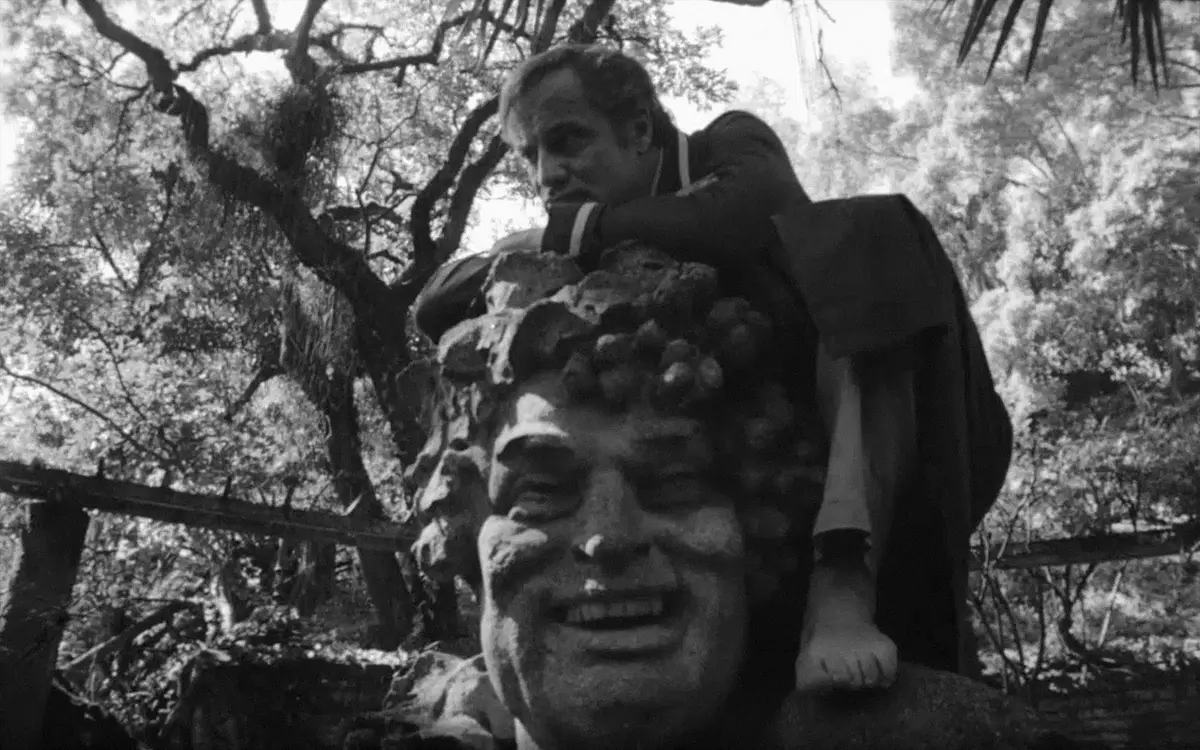 Кадр из фильма «Земля в трансе», мужчина облокачивается на голову статуи