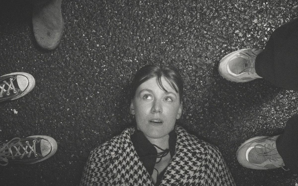 Девушка лежит на асфальте и смотрит на окружающих ее людей