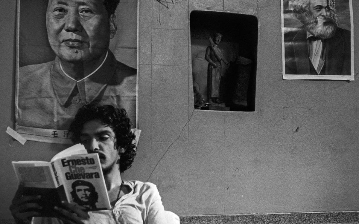 Кадр из фильма «Вернуться домой», мужчина читает книгу о Че Геваре но фоне портретов известных коммунистов