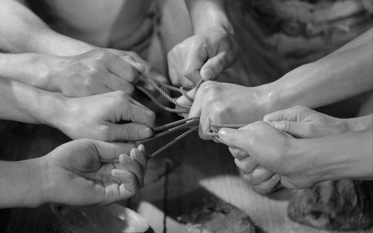 Титульное изображение для страницы события: кадр из фильма «Сага об Анатаане», четыре пары рук тянут друг у друга веревочки