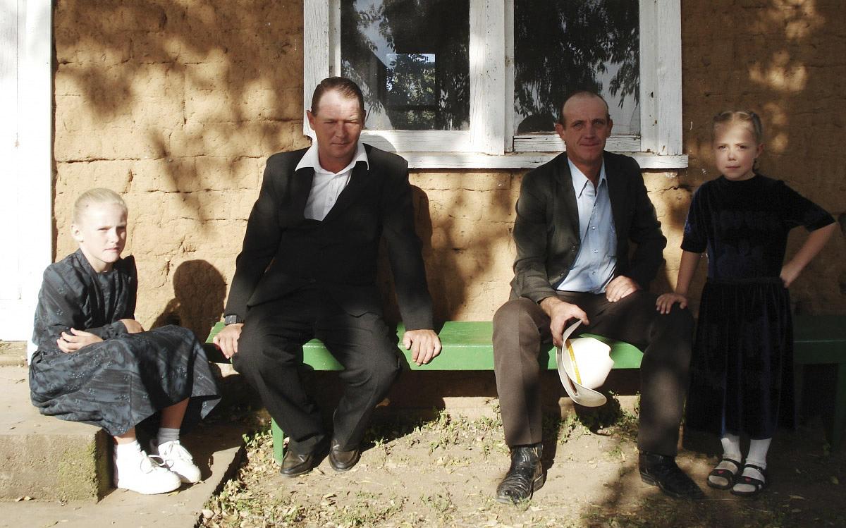 Титульное изображение для страницы события: кадр из фильма «Безмолвный свет», два мужчины, мальчик и девочка сидят на лавочке под окном дома