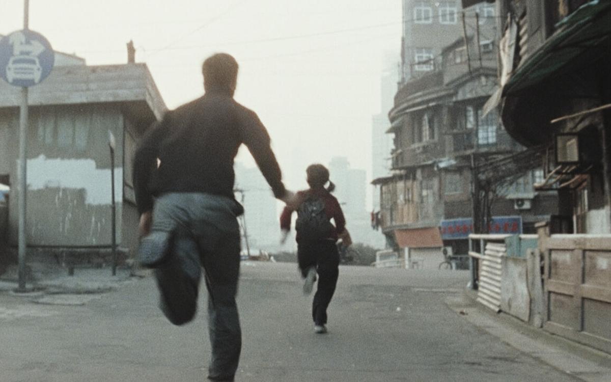 Титульное изображение для страницы события: кадр из фильма «Тайна реки Сучжоу», мужчина бежит за женщиной по серой улице