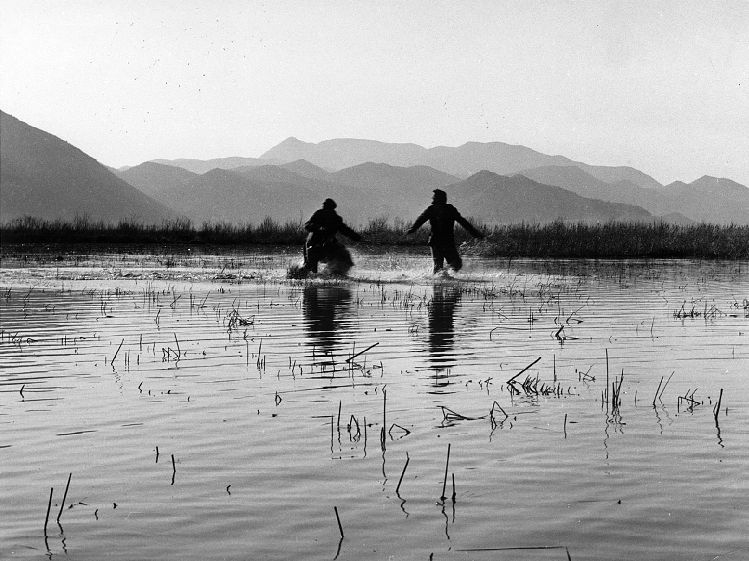Два человека сражаются посреди воды на фоне гор