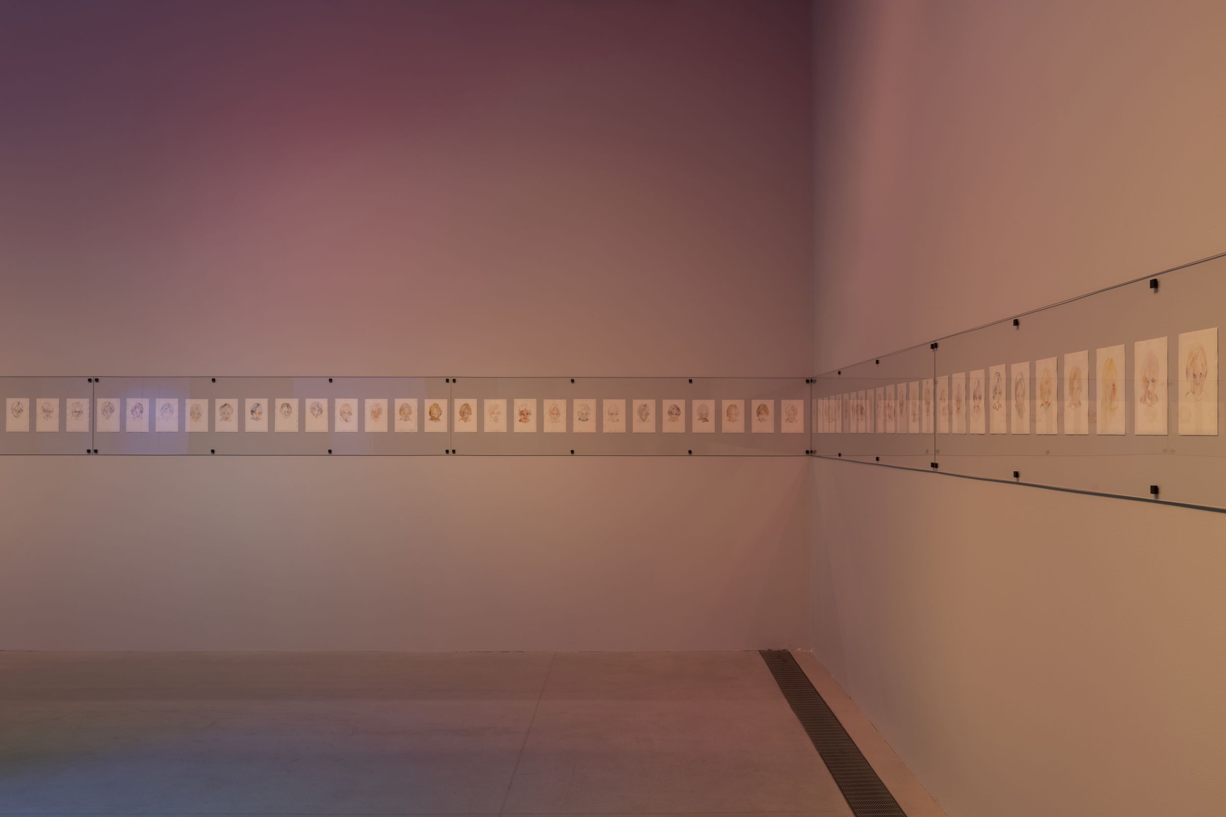 Фотография длинной серии рисунков, развешенных горизонтально по двум стенам под стеклом