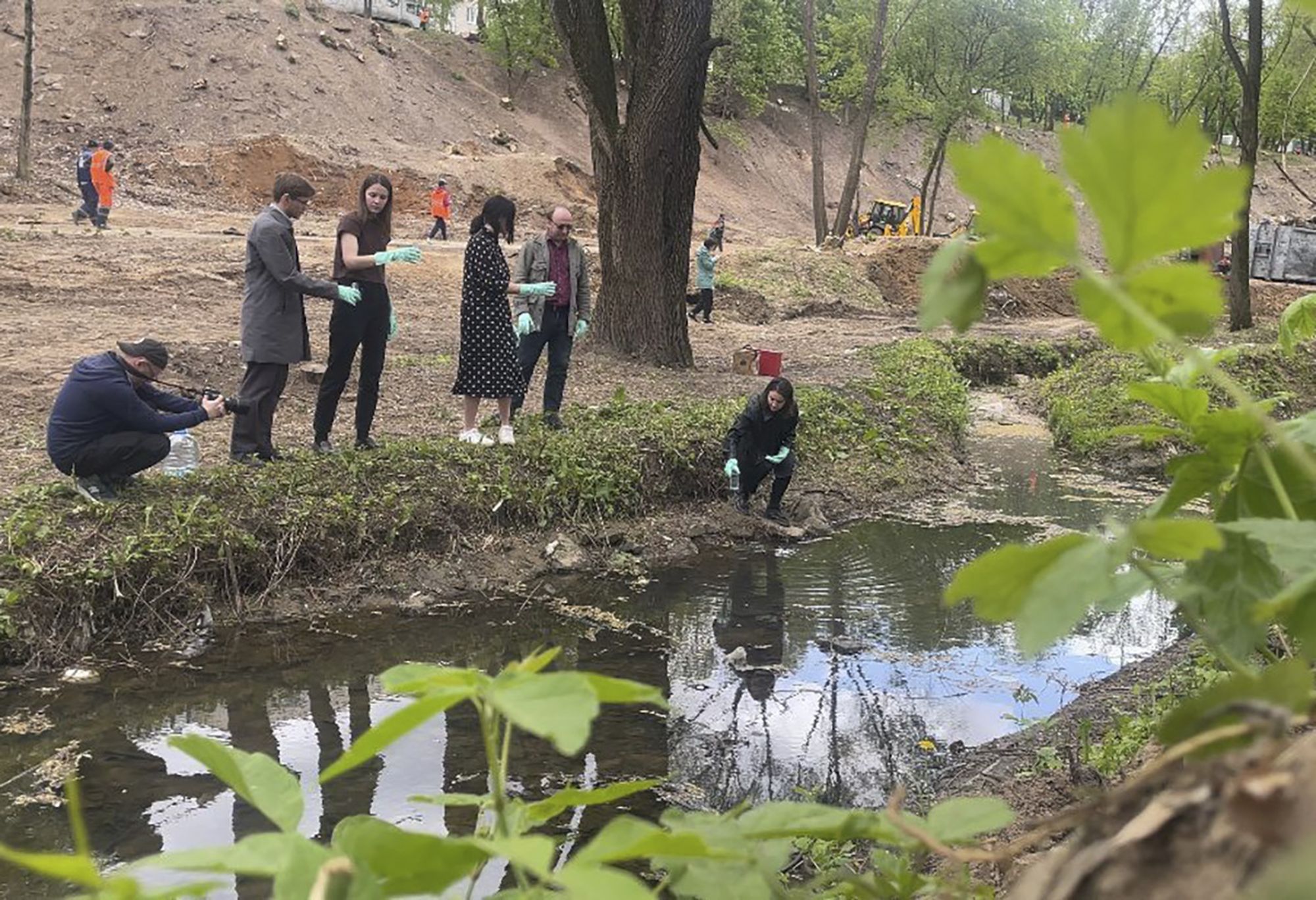 Группа людей на берегу озера в печатках берут пробы воды