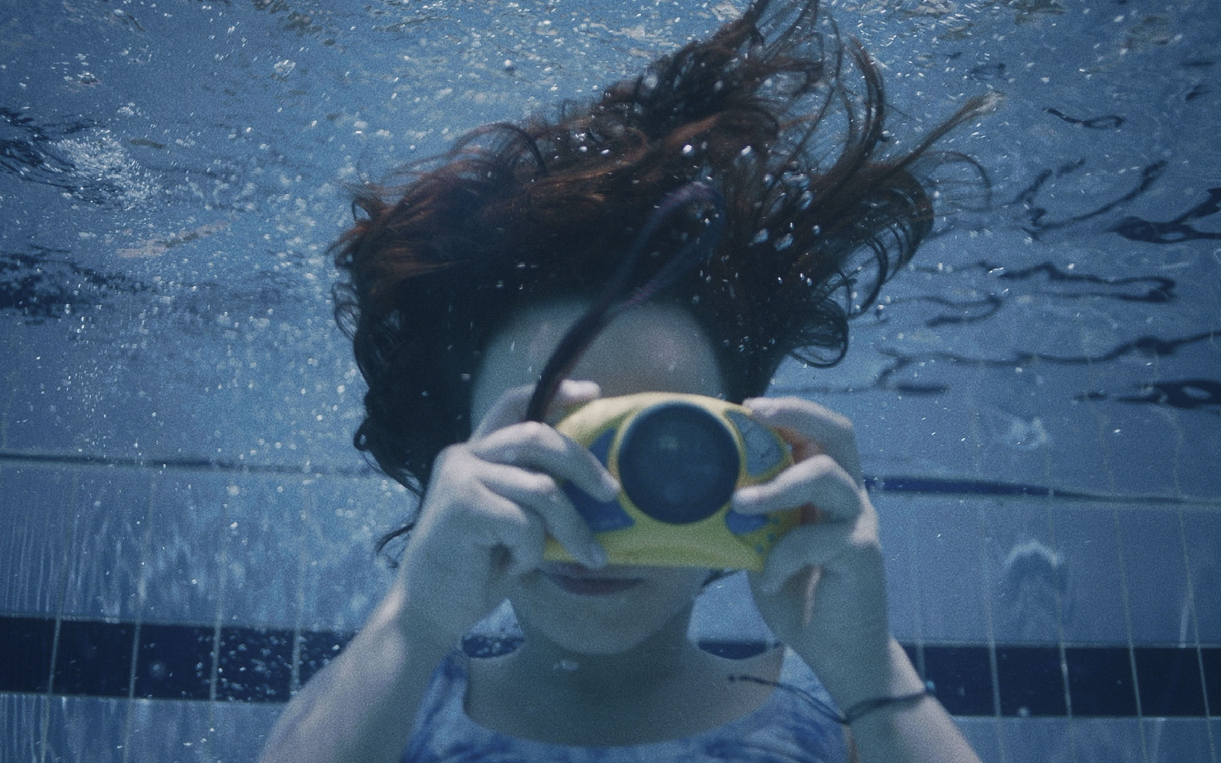 Девочка под водой в бассейне делает снимок на фотокамеру
