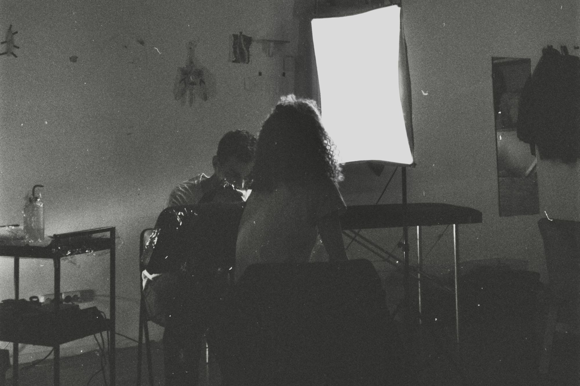  Черно-белое пленочное фото, женщина сидит спиной, перед ней мужчина набивает ей на руке татуировку